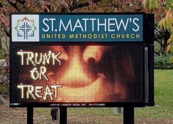 A digital sign for St. Matthew’s United Methodist Church displays “Trunk or Treat” in spooky letters with an image of a glowing jack-o’-lantern beneath autumn leaves.